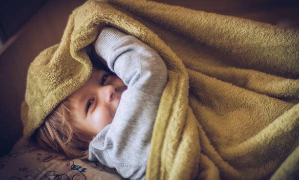 Happy child peeking out from a warm, cozy yellow blanket.