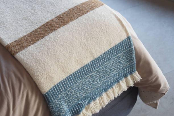 Cozy cream, brown, and blue patterned blanket with fringes draped on a bed.