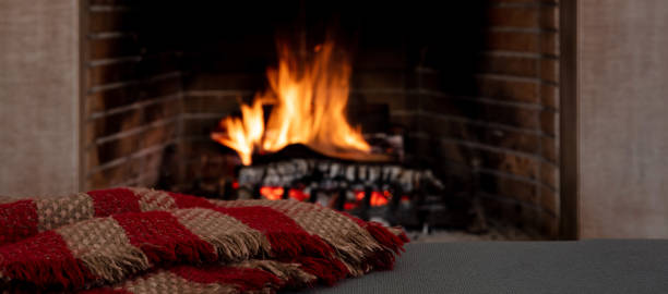 Cozy fireplace with a roaring fire and a red and brown patterned blanket.
