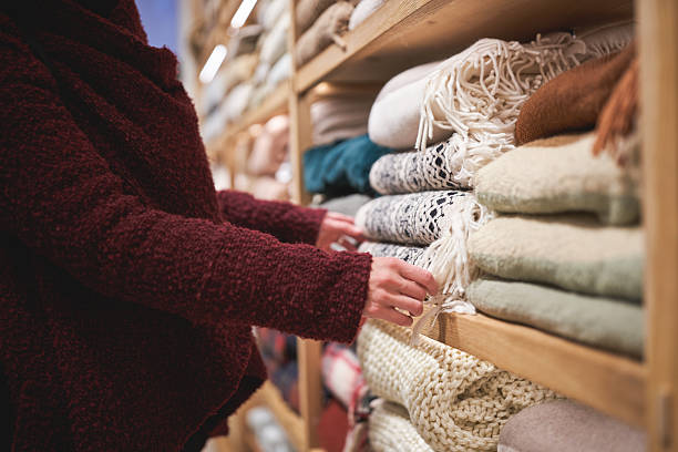 Person browsing folded blankets on shelves in a store, reaching for a soft woven blanket.