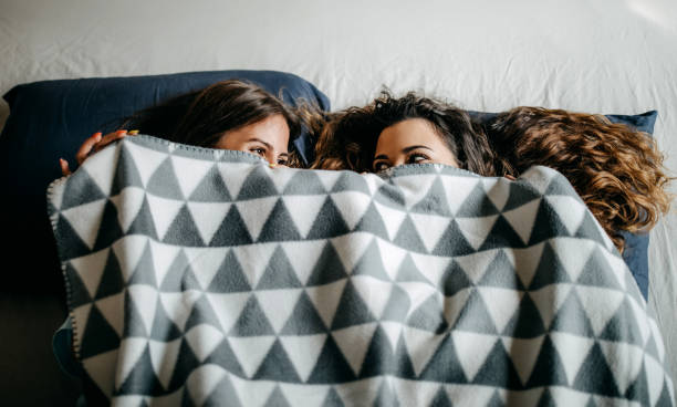 Two women peeking from under a stylish geometric patterned blanket in bed.