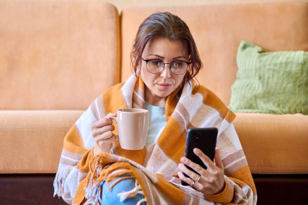 Woman relaxing with coffee, using phone, cozy in a warm striped blanket.