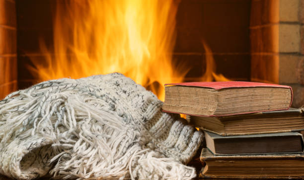Warm fireplace with a white knitted blanket and a stack of old books.