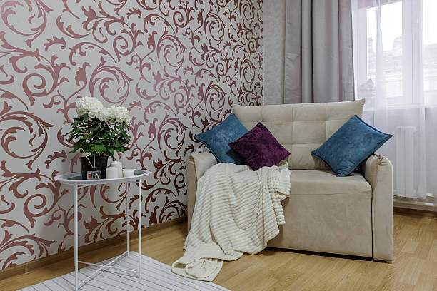 Stylish living room with a beige sofa, patterned wallpaper, and soft knitted blanket.