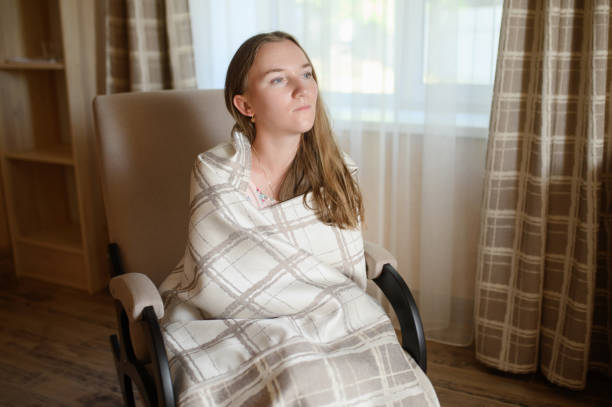 Woman wrapped in a warm plaid blanket, sitting thoughtfully in a rocking chair.