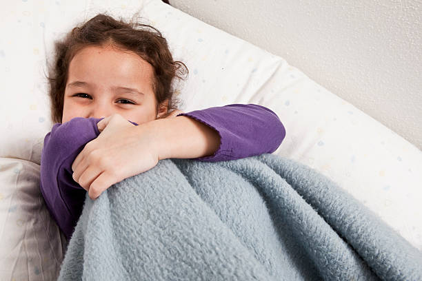 Happy young girl snuggled under a soft blue blanket in bed.