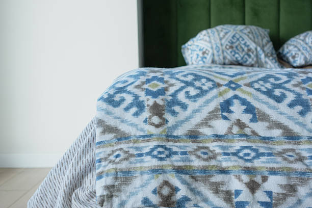 Vibrant blue and white patterned blanket on a bed with a green velvet headboard.