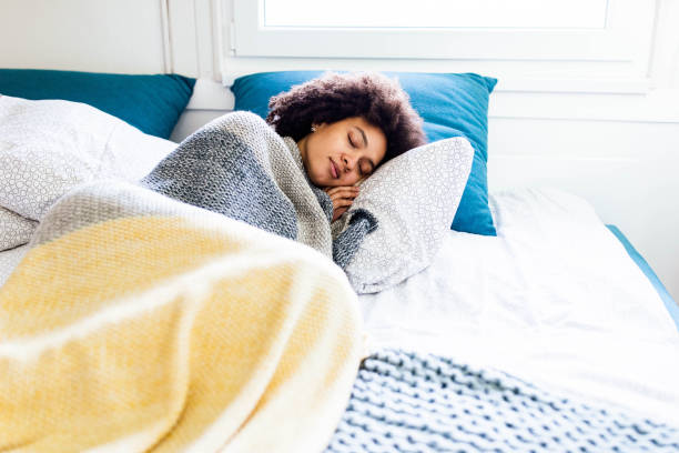 Young woman sleeping peacefully under a warm, textured yellow and grey blanket.