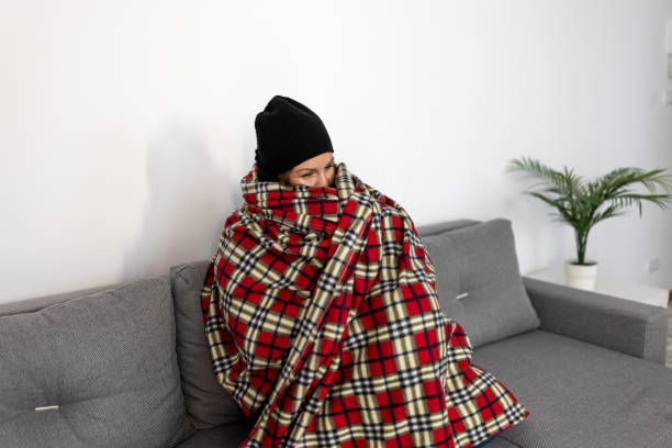 Woman in beanie, tightly wrapped in a warm red plaid blanket on a sofa.