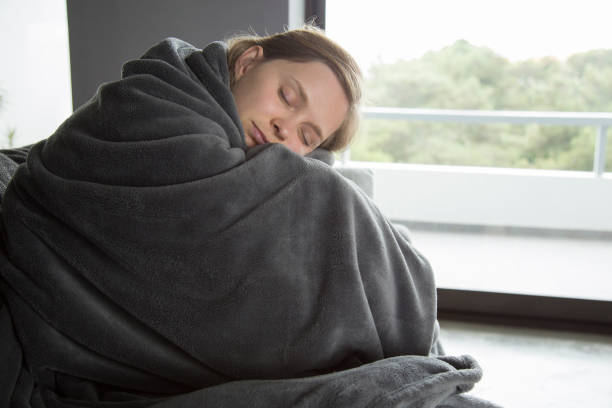 Peaceful woman wrapped in a soft, dark gray blanket, sleeping by the window.