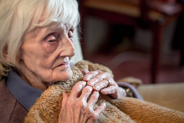 Elderly woman looking pensive, clutching a soft, comforting brown blanket.