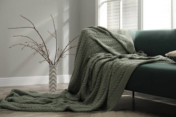 Stylish dark green sofa draped with a large, cozy cable-knit blanket in a modern living room.
