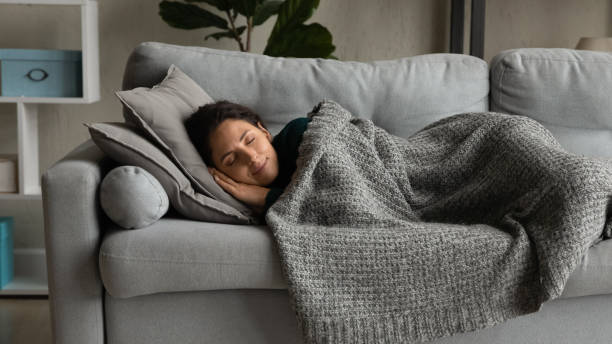 Woman napping peacefully on a sofa, covered by a textured grey blanket.