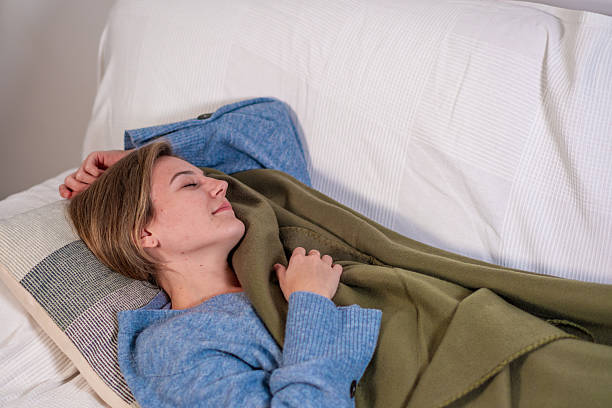 Comfortable woman sleeping peacefully on a couch, covered warmly by a green blanket.