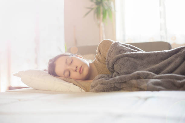 Teenager sleeping soundly under a soft grey blanket, enjoying a peaceful morning nap.