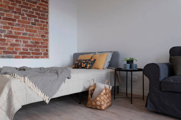 Minimalist bedroom with a single bed, brick wall, and a woven patterned blanket.