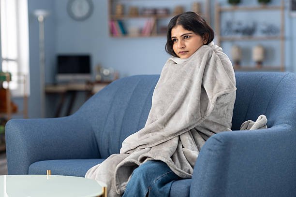 Young woman on a couch, bundled snugly in a soft grey blanket.
