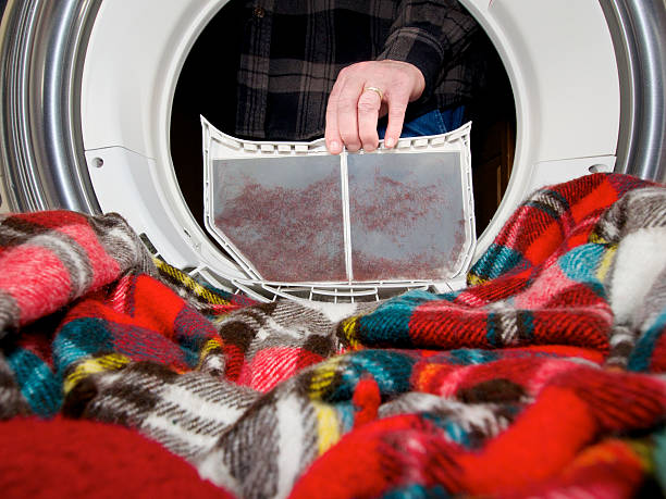 Person cleaning dryer lint trap after drying a colorful plaid blanket.