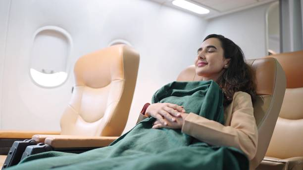 Woman sleeping comfortably with a green blanket on a plane.