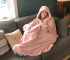 Happy woman in a comfy pink hooded wearable blanket relaxing on a couch.