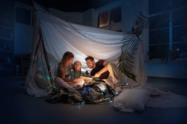 Family enjoying story time together inside a magical blanket fort with fairy lights.