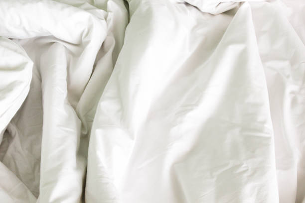 Crumpled unmade white bed sheets or a lightweight blanket with many wrinkles.