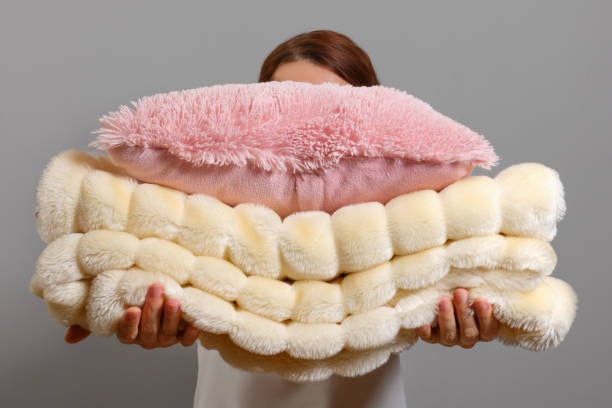 Person holding a soft pink pillow and a fluffy cream-colored textured blanket.