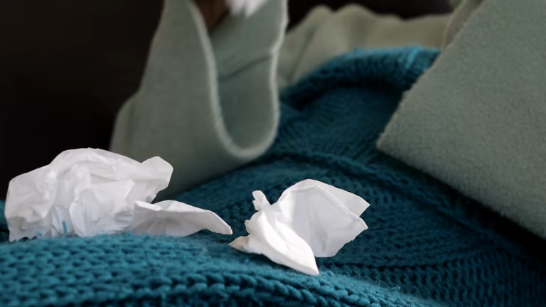 Used tissues scattered on a warm, blue knitted blanket, symbolizing illness.