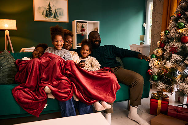 Happy family snuggled under a red blanket on a couch with a Christmas tree.