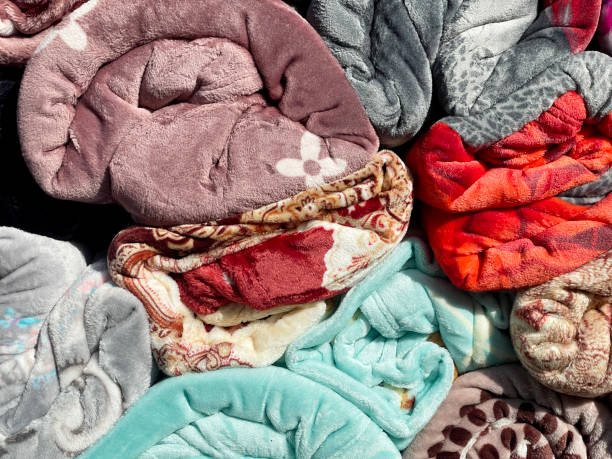 A close-up of many soft, colorful, patterned fleece blankets piled together.