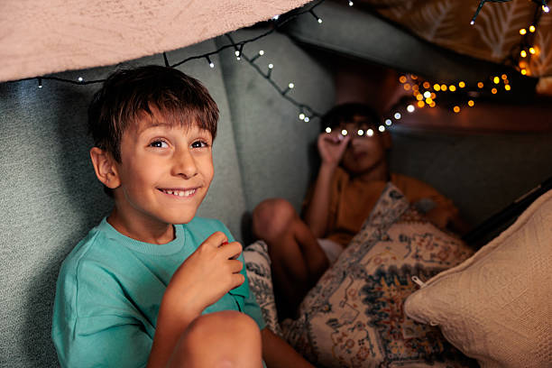 Two cheerful boys having fun playing together inside their homemade blanket fort.
