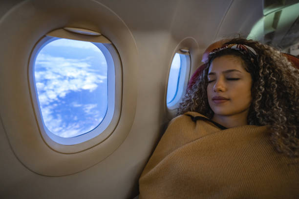 Woman with curly hair sleeping peacefully under a brown blanket by the window.